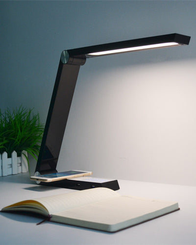 A wireless charging desk lamp in black next to a book