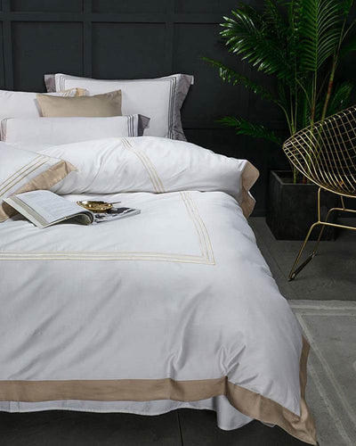 Casablanca bedding in white and gold presented on a bed in front of a grey wall 