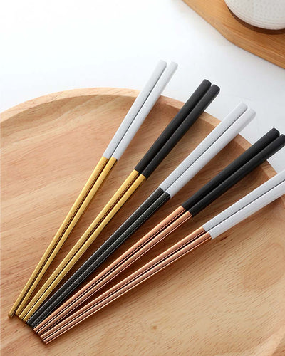 Chopsticks in golden and rose gold colors with a black or white stick on a wooden plate