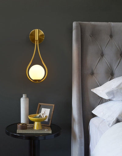 Golden wall lamp hanging in a bedroom next to a bed and a night desk