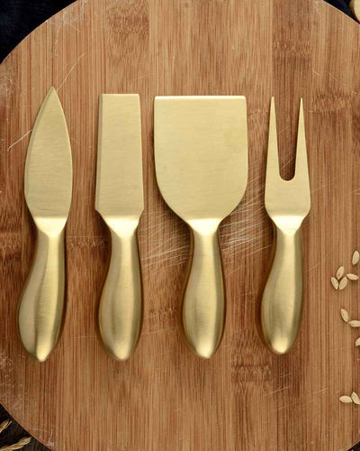Cheese set of scraper, spatula, knife and fork made of gold and stainless steel on a wooden plate
