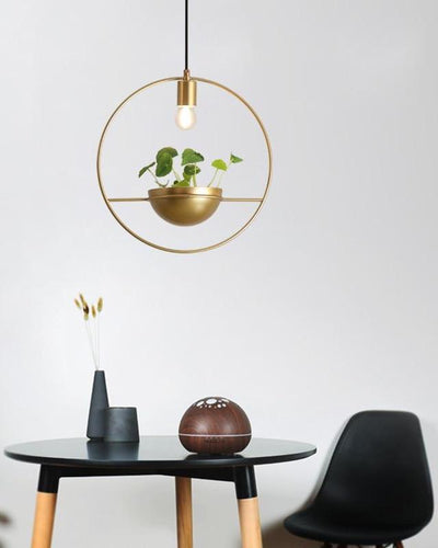A golden ceiling lamp with a plant in it hanging over a black table and a black chair on white background