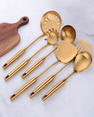Kitchen utensils including spatula, ladle, spoon, pasta server and a skimmer in gold color on white background