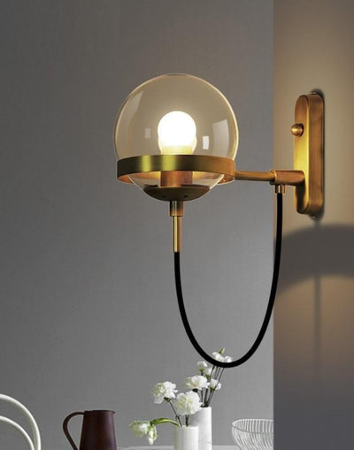 A nordic wall lamp made of bronze hanging on a grey wall next to white flowers