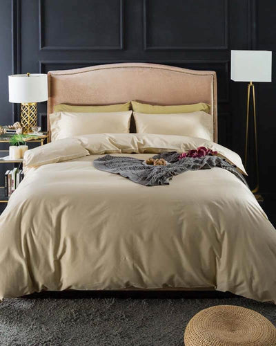 Portobello Bedding in a slight vanilla color covering a rosé colored bed in front of a grey wall 