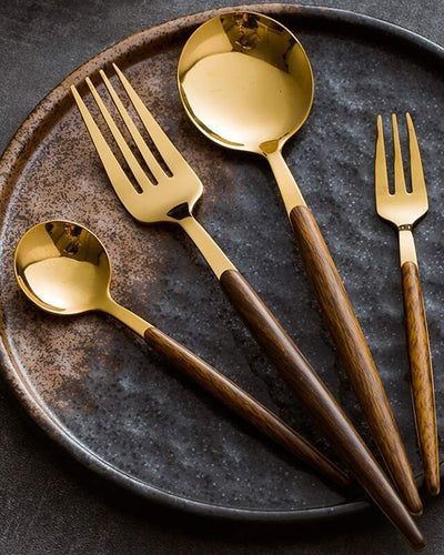 Cutlery set in golden color and wooden ending on a marble plate